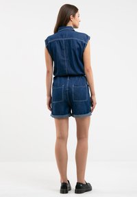 Džinsinis rompers su trumpomis rankovėmis, užpakalinėmis kišenėmis ir suktomis hemomis. Tamsiai mėlyna spalva su kontrastingomis siuvimo detalėmis. Lygi tekstūra.