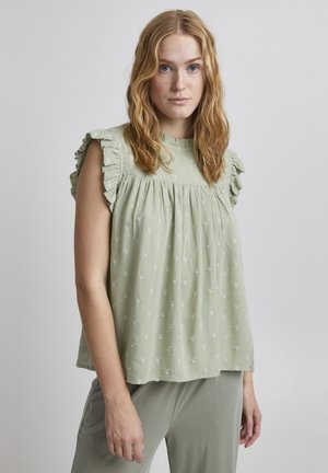 Hellgrünes Tanktop aus strukturiertem Stoff, mit Rüscheärmeln und gerafftem Design, verziert mit kleinen, kreisförmigen Mustern.