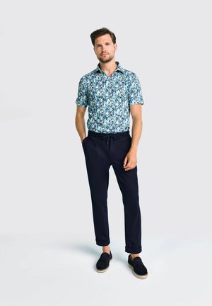 Kurzarmhemd mit einem blauen Blumenmuster, kombiniert mit marineblauen Hosen und marineblauen Slippern. Aus Baumwollmaterial, legerer Schnitt.