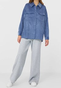 Himmelblaues Wildlederhemd mit Knöpfen und zwei Brusttaschen, kombiniert mit hellgrauen, weit geschnittenen Jogginghosen und weißen Turnschuhen.