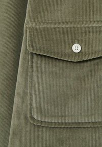 Țesătură de catifea în tonuri de verde măsliniu, cu o buzunar frontal prevăzut cu un capac rotunjit și închidere cu un nasture alb, evidențiind o textură verticală cu nervuri.