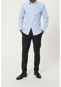 Ljusblå långärmad skjorta med knappar och klassisk krage, kombinerad med svarta byxor och svarta finskor. Släthemd tyg, skräddarsydd passform.