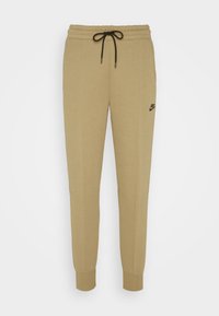 Tan Nike joggers med dragsko i midjan, insvängda ben, sidofickor och logodetaljer i svart på höfterna. Mjuk, bomullsblandat material.