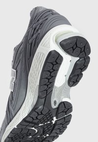 Męskie buty do biegania z szarym siateczkowym wierzchem, amortyzowanym piętą i czarną gumową podeszwą z bieżnikiem zapewniającym przyczepność.