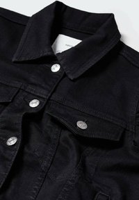 Giacca in denim nero con colletto a punta, bottoni a pressione argentati, due tasche sul petto e tessuto texturizzato con dettagli di cucitura visibili.