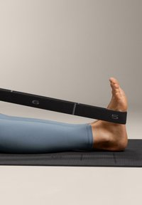 Čierny odporový pás obtočený okolo nohy, ležiaci na čiernej cvičebnej podložke. Dolná časť nohy je pokrytá svetlomodrou látkou.