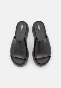 Sandales noires à glissière avec une tige synthétique brillante et une semelle texturée, dotées d'une large sangle et d'un design de semelle plate pour le confort.