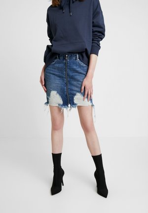 Blå denim mininederdel med slidte pletter og frynset kant, kombineret med en mørk hættetrøje og sorte spidse ankelstøvler.