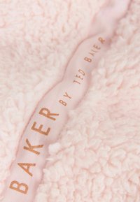 Jasnoróżowy, miękki materiał o teksturowanej powierzchni z puszystą fakturą. Posiada wstążkową metkę z napisem "BAKER by TED BAKER" w złotym kolorze.