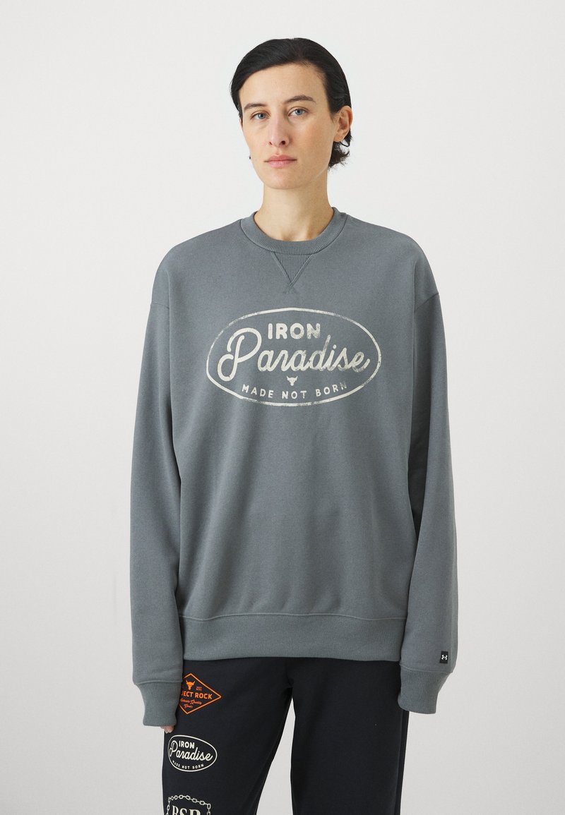 Grå crewneck sweatshirt med hvit "IRON Paradise" tekst. Myk stoff, ribbestrikkede mansjetter og halslinning, avslappet passform. Kombinert med mørke bukser med lapper.