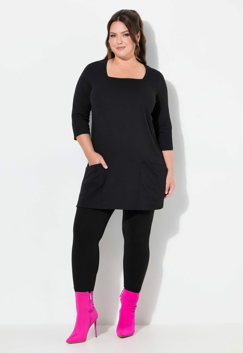 Vestito tunica nero con scollo quadrato, maniche a tre quarti, tasche frontali, abbinato a leggings neri e stivaletti alla caviglia rosa.