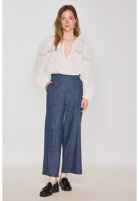 Blusa bianca a maniche lunghe con righe verticali e dettagli in pizzo, abbinata a pantaloni in denim scuro a gamba larga e mocassini neri.