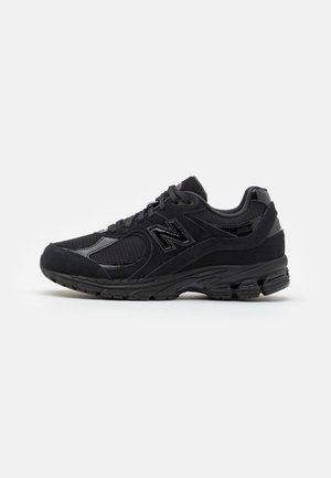 Baskets noires New Balance 2002R avec superpositions en mesh et daim, fermeture à lacets, semelle amortissante et logo de la marque sur le côté.