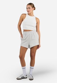 Biely rebrovaný crop top, šedé šortky s elastickým pásom, biele ponožky s čiernym písmom a šedé/čierne tenisky. Jednoduché, neformálne športové oblečenie.