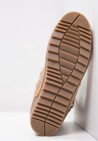 Hnědá gumová podrážka s hlubokými drážkami pro lepší přilnavost. Svršek má hladký povrch a vyšívané detaily. Zaoblený tvar s minimálním brandingem.