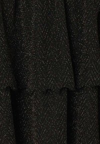 Tissu noir avec un motif en chevrons, ornés d'accents en paillettes métalliques, créant une apparence texturée et superposée.