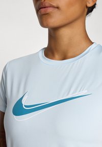 Lyseblå idretts T-skjorte med korte ermer, med en stor turkise og hvit swoosh-logo over brystet. Glatt stoffoverflate.