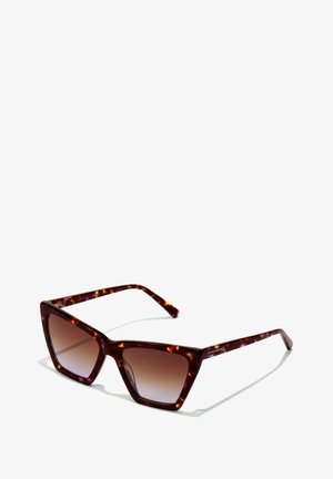 Kilpkonnakujulised päikeseprillid, millel on nõgusad pruunid objektiivid. Julge, nurkadega raamidisain ja sile viimistlus. Kaubamärgi logo templitel.