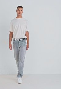 Lichtgrijze corduroy broek, casual witte t-shirt, zwart-wit grafische riem en witte sneakers. Eenvoudig ontwerp en aangesloten silhouet.