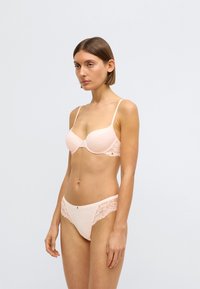 Σετ ροζ ελαφριάς εσώρουχης με στηθόδεσμο με επένδυση και λεπτομέρειες από δαντέλα, συνοδευόμενο από εσώρουχα με floral δαντέλα και μικρή μεταλλική διακοσμητική λεπτομέρεια.