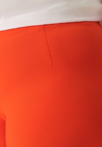 Rote Stoffhose mit glattem, strukturiertem Finish. Verfügt über eine dezente Rückennaht als Designelement.