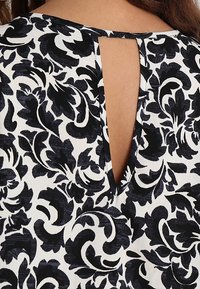 Bloementop in zwart en wit, met een sleutelgatdetail achteraan, van een soepele textuur en zachte stof.