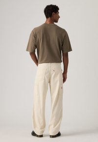 Φωτεινό μπεζ παντελόνι με λεπτές ρίγες και πλαϊνές τσέπες, σε συνδυασμό με κοντομάνικη πράσινη-ελιά μπλούζα, φορεμένα από πίσω.