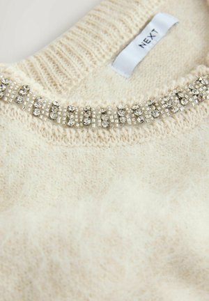 Cremefarvet strikket sweater med en tekstureret overflade og en krave med glitrende perledetaljer. Mærket viser brandnavnet "NEXT."
