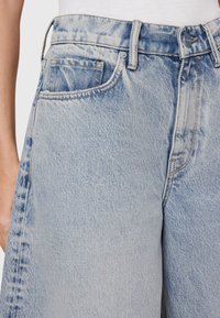 Gli shorts in denim azzurri chiari presentano una vita alta, cuciture visibili, tasche anteriori e posteriori, e una texture leggermente sbiadita.