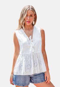 Witte mouwloze top met een V-hals en strikdetail, voorzien van bloemembroidery en een geraffineerde zoom, gecombineerd met denim short.