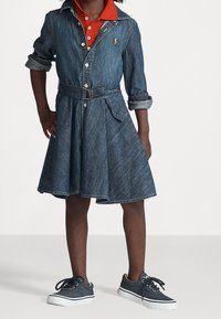 Jeanklänning med korta ärmar, bälte i midjan och utsvängd kjol. Kombinerad med grå sneakers och en röd skjorta med krage under.