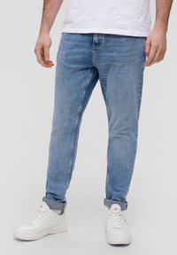 Jasnoniebieskie dżinsy o zwężanym kroju, z klasycznym pięciokomorowym fasonem i widocznym przeszyciem. Połączone z białymi sneakersami.