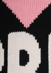 Nahaufnahme eines gestrickten Stoffes mit einem rosa Herz und schwarzen und weißen Buchstaben auf einem schwarzen Hintergrund.