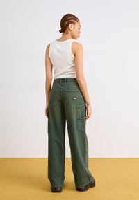 Pantaloni cargo verzi cu picioare largi, multiple buzunare, textură de denim, design cu talie înaltă și o aplicație pe spate. Top ajustat alb fără mâneci.