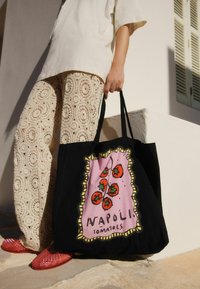 Black tote bag featuring a pink graphic design with red tomatoes and the text "NAPOLI TOMATOES." Made of fabric, it has sturdy handles.