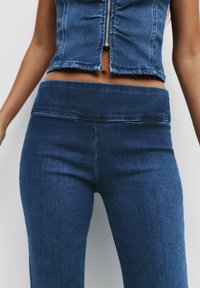 Leggings en denim bleu foncé, dotés d'une taille haute, d'une texture lisse et de détails de couture minimaux. Design classique ajusté.