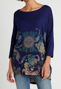 Haut bleu marine avec des manches trois quarts, présentant un imprimé floral et cachemire coloré à l'ourlet. Tissu doux avec une coupe décontractée.