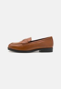 Mocasines de cuero marrón con punta redondeada, costuras detalladas y una pequeña correa superior. Presentan una suela de goma negra y una textura suave.