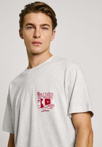Gray cotton t-shirt featuring a red graphic design with a retro computer and keyboard. Short sleeves and a crew neckline.