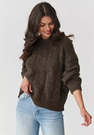 Brązowy sweter dzianinowy z prążkowanym okrągłym dekoltem i długimi rękawami, z teksturowanym wykończeniem i lekko skróconym krojem. Połączony z jasnymi dżinsami.
