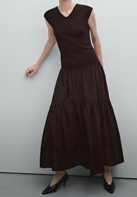 Mustapuku, jossa on istuva bodice ja kerroksellinen, virtaava hame. Valmistettu pehmeästä kankaasta, lyhyillä hihoilla ja V-pääntiellä.