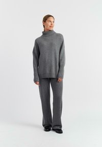 Maglione grigio a maglia con collo alto e vestibilità tranquilla, abbinato a pantaloni larghi coordinati, tutti realizzati in tessuto morbido.