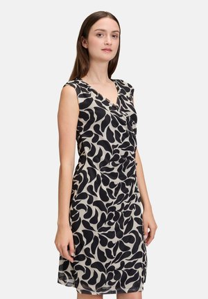 Mouwloze jurk van een luchtige stof met een zwart en beige bladerenprint, voorzien van een v-hals en ruches in de taille.