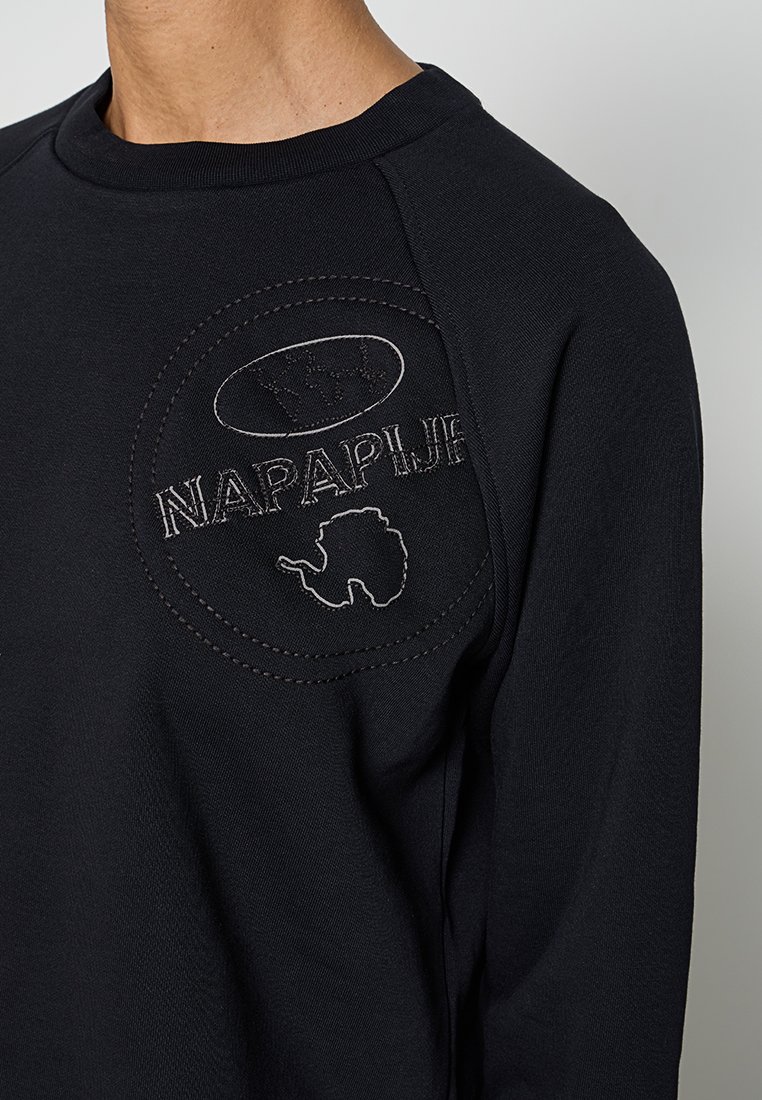 Schwarzer Sweater mit einem kreisförmigen gestickten Logo mit "NAPAPIJRI" und einem Kartendesign. Hergestellt aus weichem, strukturiertem Material mit Raglanärmeln.