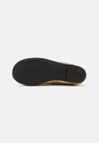 Zapato de ballet texturizado en oro con una suela negra flexible, presentando una punta redondeada y una impresión del logo en la parte inferior.