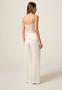 Satijnen roze camisole met dunne bandjes, gecombineerd met hoog- taille witte linnen broeken met een losvallende pasvorm en zijzakken.