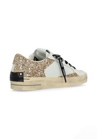 Sneaker con una base in pelle bianca, glitter dorato sul tallone, accenti neri e lacci rotondi. Suola testurizzata con dettagli di cucitura visibili.