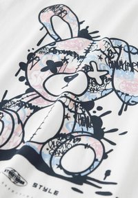 Hvid t-shirt med et grafisk design af en stiliseret bjørn i sort, blå og pink, med abstrakte mønstre og sprøjtede detaljer.
