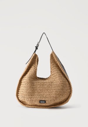 Καφέ υφαντή τσάντα ώμου με μαύρο ρυθμιζόμενο ιμάντα και μικρό μαύρο λογότυπο DKNY στο μπροστινό μέρος, τοποθετημένη σε απλό φωτεινό φόντο.