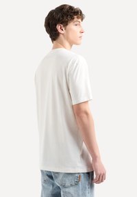 T-shirt leggero beige a maniche corte realizzato in tessuto morbido, con scollatura a girocollo e vestibilità rilassata, mostrato di spalle.